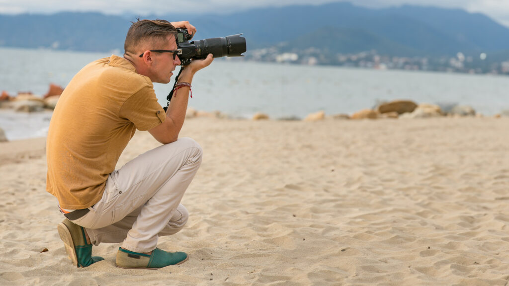 Fotógrafo en la playa capturando una escena con cámara profesional en un entorno natural y relajado.