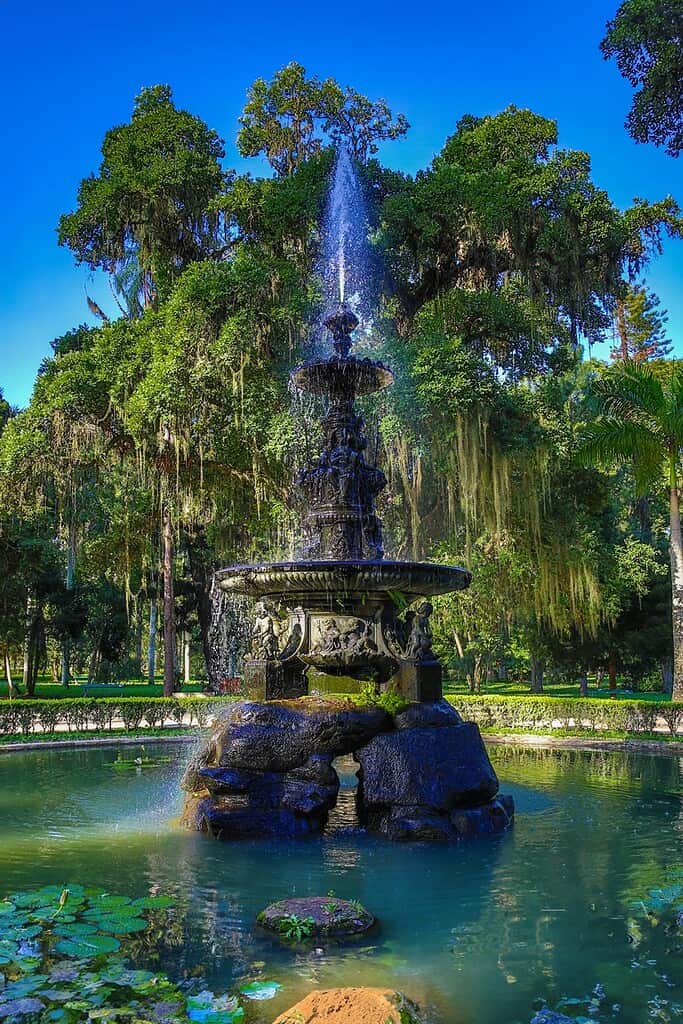 Fuente de agua en parque con árboles verdes y cielo azul, ideal para soluciones innovadoras en gestión de espacios públicos y sostenibilidad ambiental en solucionesait.com.