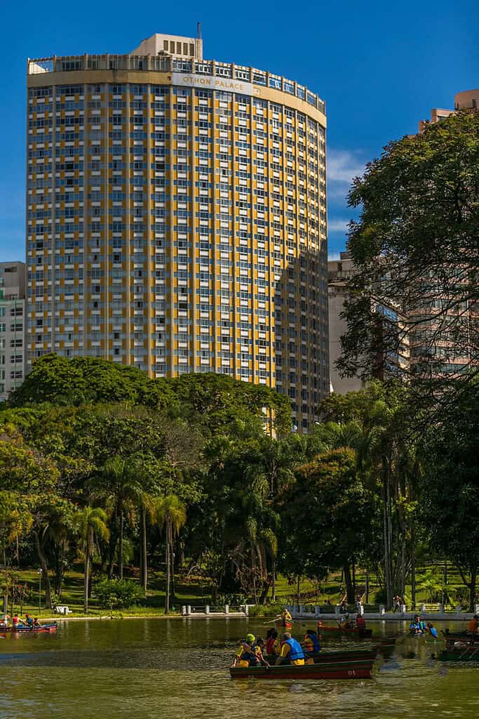 Othon Palace en Guadalajara, edificio alto con arquitectura moderna y ventanas distintivas, rodeado de áreas verdes y un lago con personas remando, en una ciudad vibrante y llena de naturaleza.