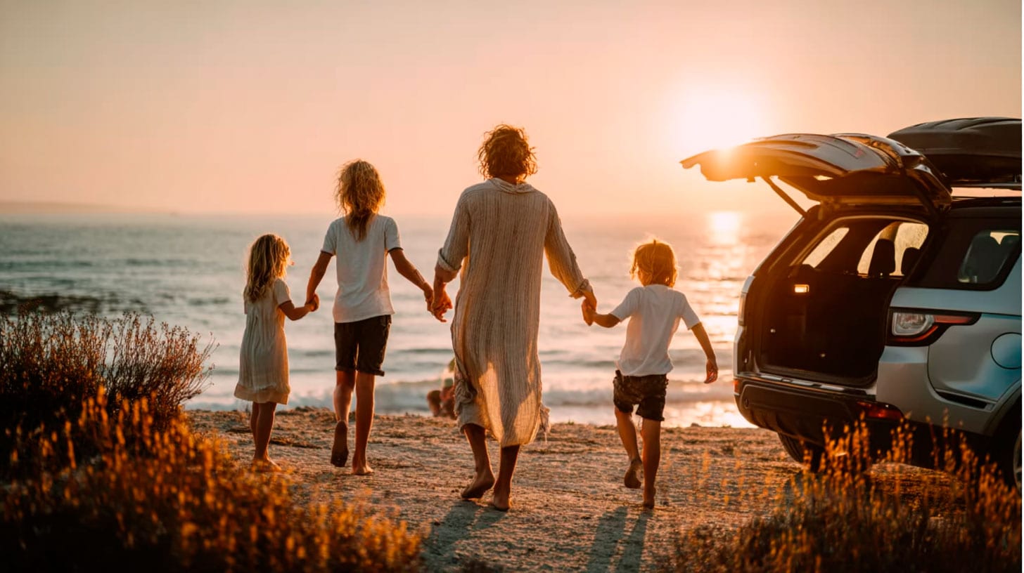 Familia disfrutando en la playa con coche y maletas, al atardecer, promoviendo soluciones tecnológicas y de movilidad para viajes familiares.